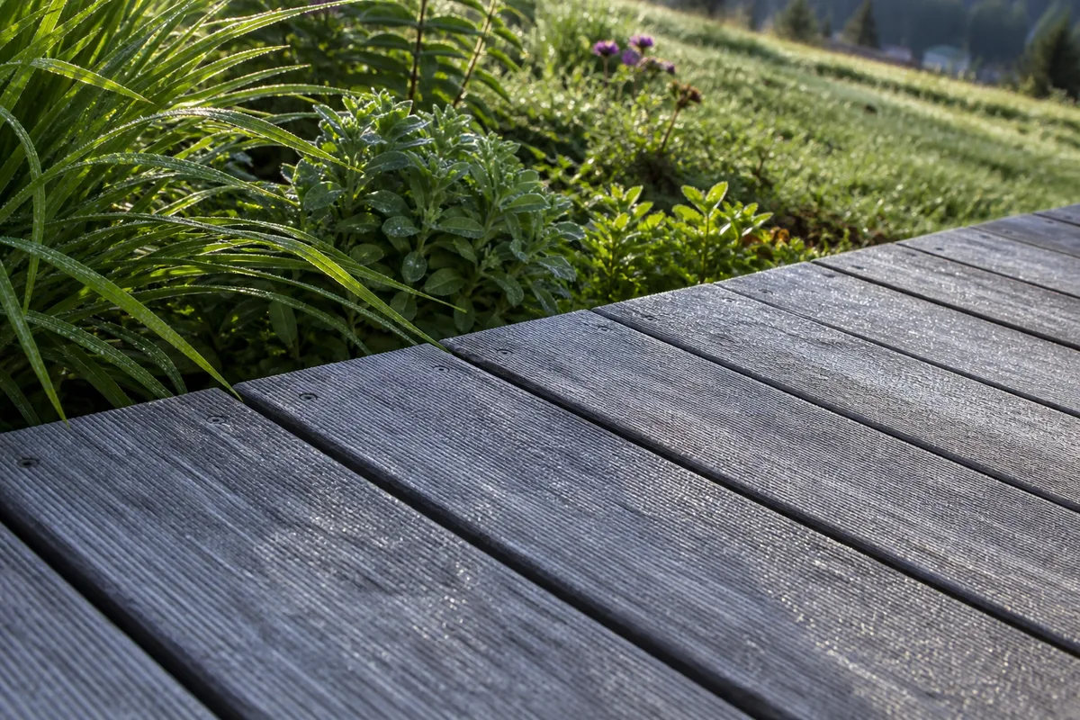 Terrasse en bois de mélèze grisé bordée d’un jardin de pente, lumière fraîche du massif vosgien